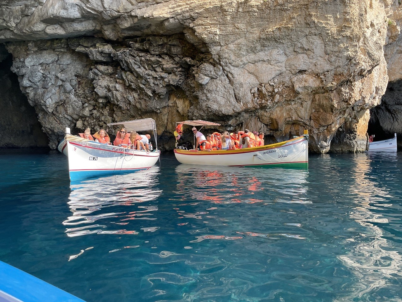 Two small boats with seven people each in orange life vests and the clear blue waters of Malta